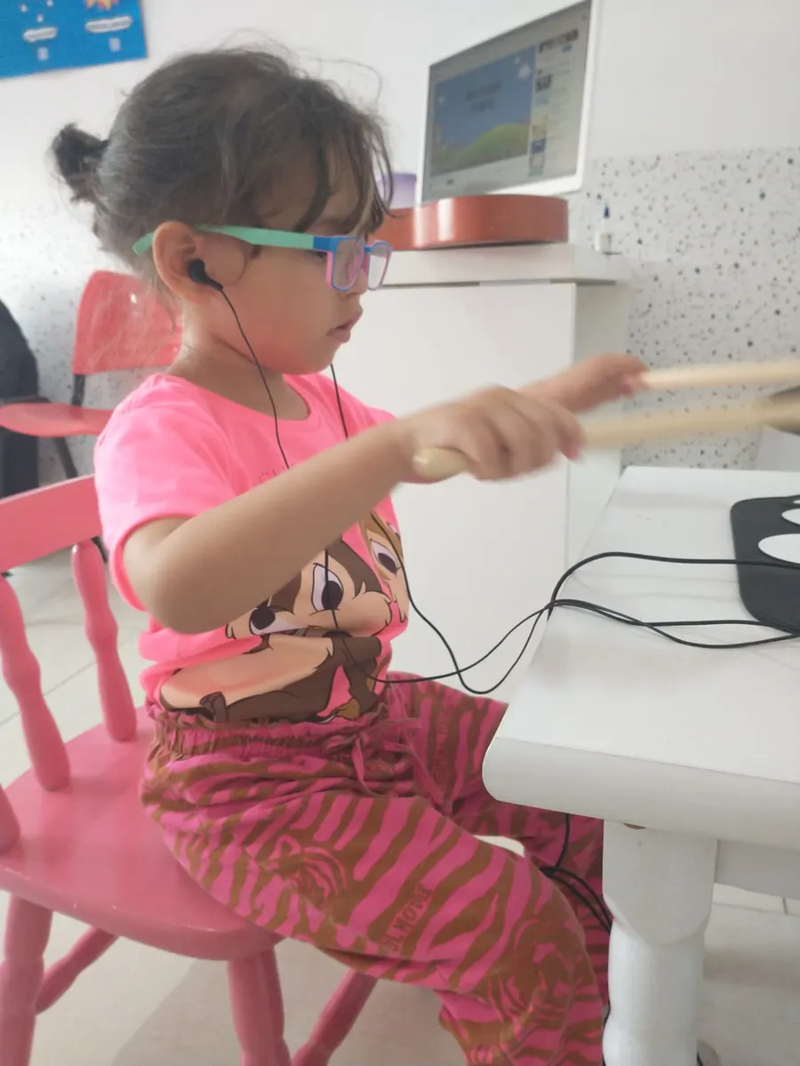Menina de fone tocando com baqueta em uma superfície, em atividade rítmica