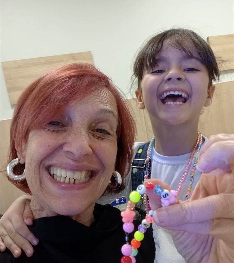 Cristiane Ruivo e uma criança atendida, as duas rindo, segurando uma pulseira de miçangas feita na sessão