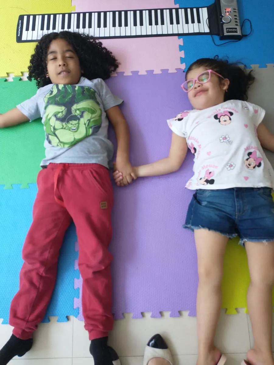 Duas crianças deitadas lado a lado de mãos dadas, ouvindo música