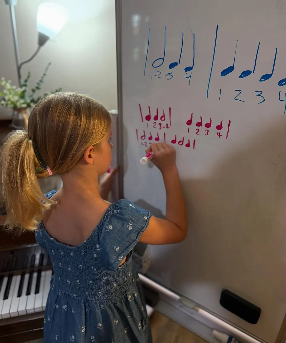 Criança escrevendo figuras rítmicas num quadro branco, ao lado de um piano