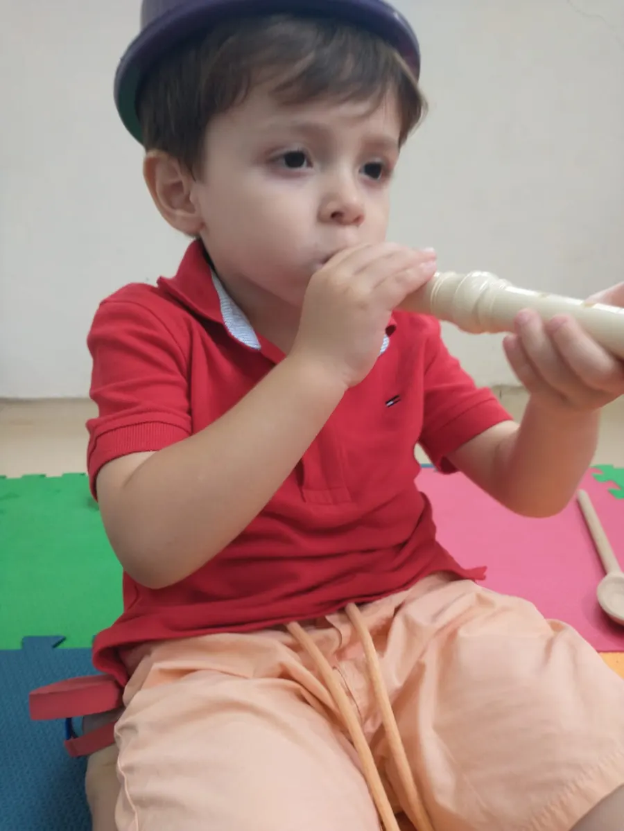 Menino soprando uma flauta doce, sentado no tapete de atividades