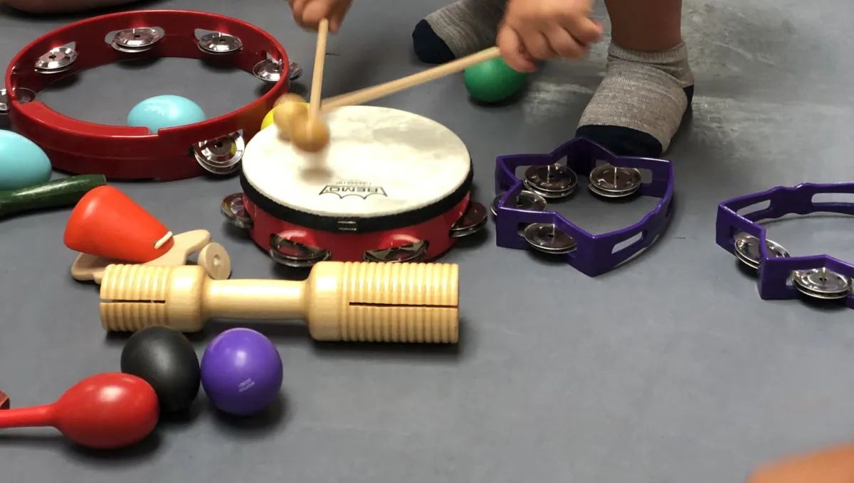 Crianças em sessão de musicoterapia em grupo, com tambor, pandeiros e chocalhos no chão