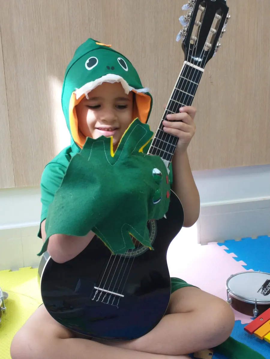 Criança com fantasia de dinossauro segurando um violão durante a sessão