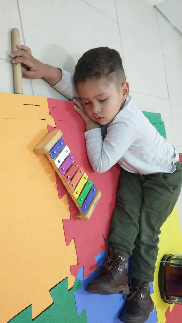 Menino deitado no chão ao lado de um xilofone, em momento de calma